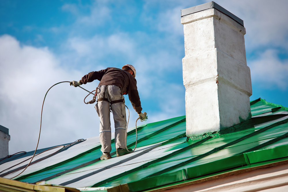 Guy painting the roof with green paint.