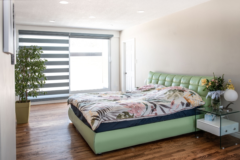 Modern bedroom featuring stylish motorised blinds for effortless light control and privacy, paired with a sleek green bed and wooden flooring.