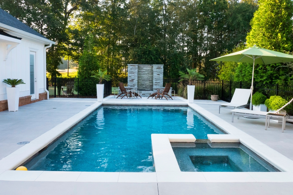 Modern outdoor space with a sleek rectangular concrete pool and integrated spa, complemented by minimalist furniture and greenery.