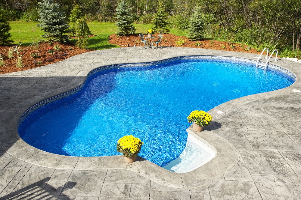 Beautifully landscaped garden with a curvy concrete pool, vibrant flowers, and a peaceful seating area for relaxation.