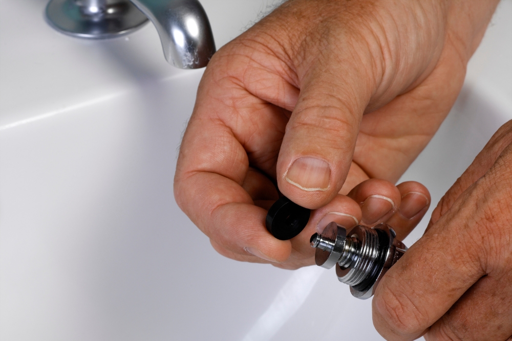 Hands of a professional plumber replacing a tap washer on a bathroom sink to fix a leak.