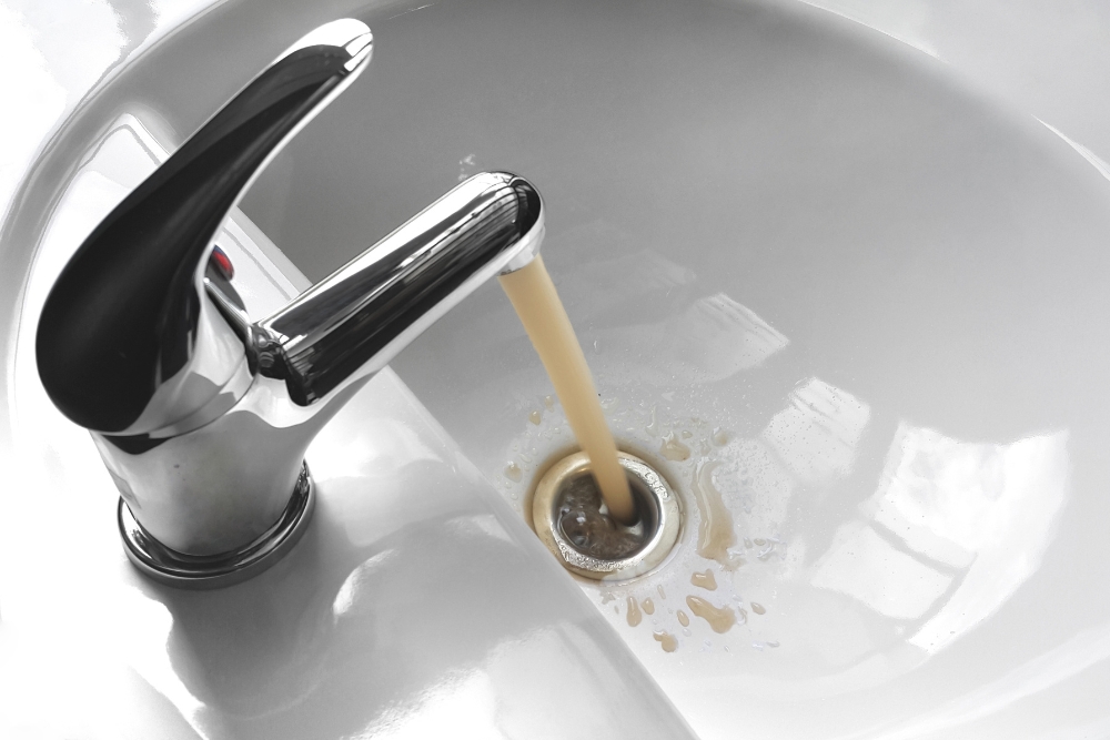 Rusty, discoloured water flowing from a bathroom tap, indicating a potential plumbing issue.