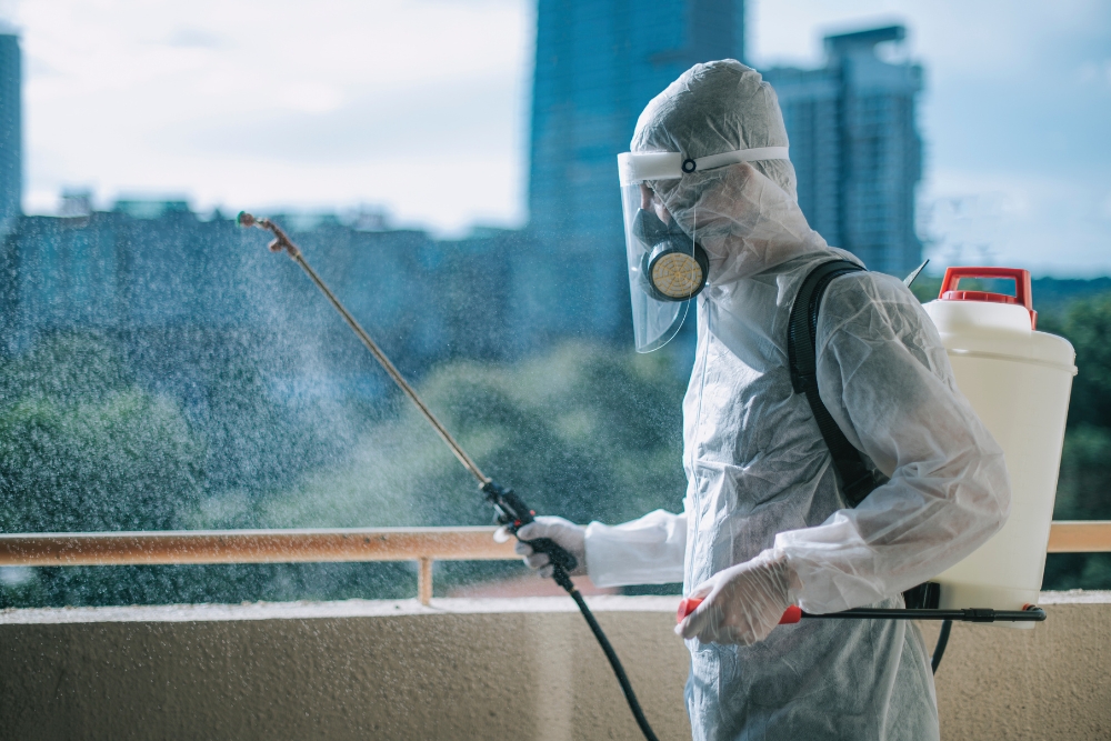 Pest control specialist spraying insecticide on a balcony with a cityscape in the background."